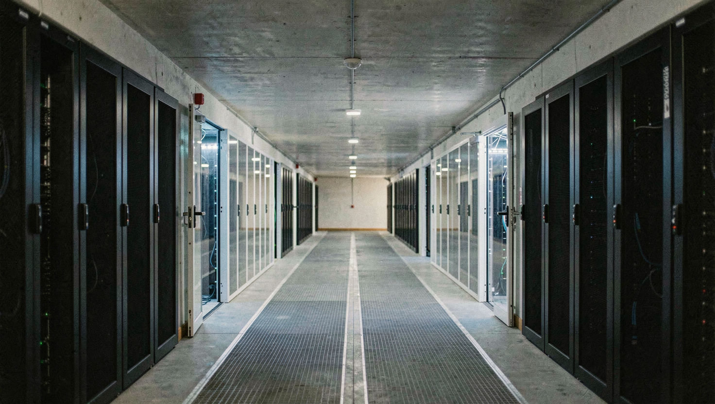 Allée froide confinée par un toit rigide et deux portes battantes transparentes, rangées de baies noires de part et d'autre, éclairage bleuté à l'intérieur du couloir, sol technique gris, cadrage en perspective centrale